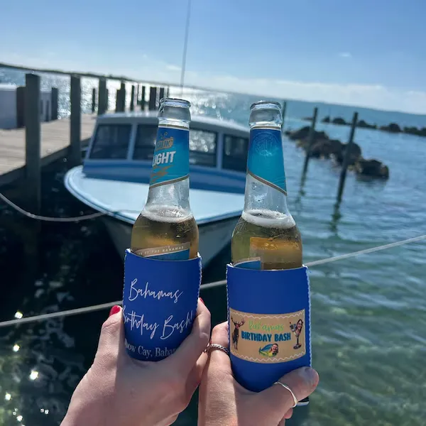 Two personalized custom beer koozies on bottles during a lakeside birthday celebration.